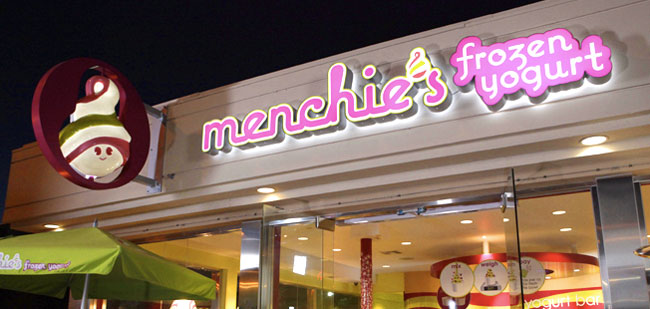 The Menchie's sign is lit up on the outside of the building at night.