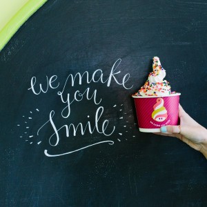 A blackboard with "We make you smile" written next to a hand holding a cup of frozen yogurt