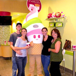 Four smiling customers flank a Menchie’s mascot inside a Menchie’s store.