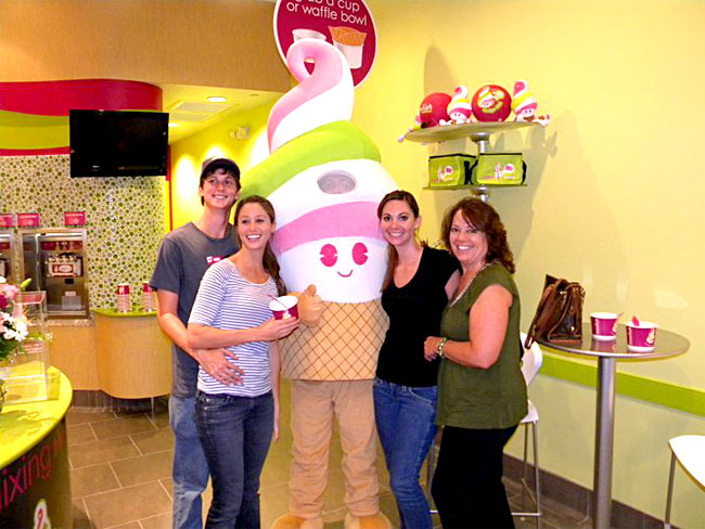 Four smiling customers flank a Menchie’s mascot inside a Menchie’s store.