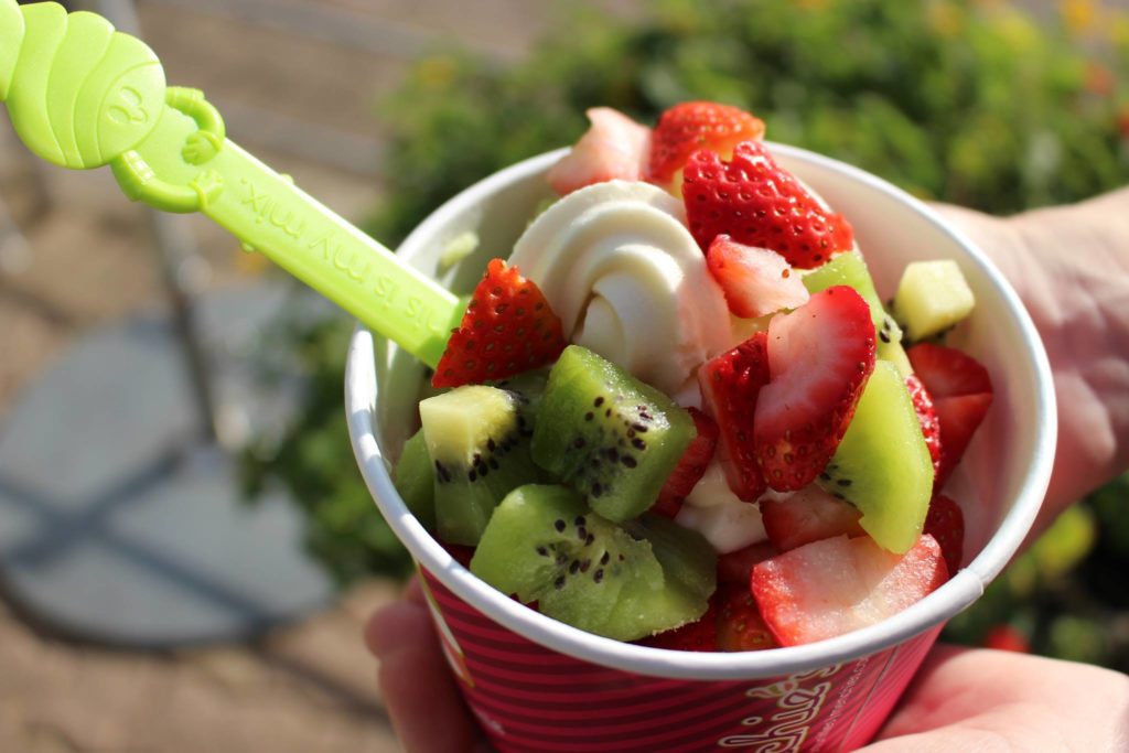 A cup of vanilla froyo topped with strawberries and kiwi.