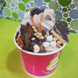 A cup of swirled frozen yogurt is topped with dark chocolate and peanut butter chips, brownie chunks and mochi candies.