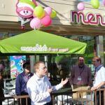 A man speaking to a crowd outside of a Menchie's store